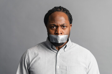 Studio shot of sad African American voiceless speechless guy looking at camera, mouth closed with...