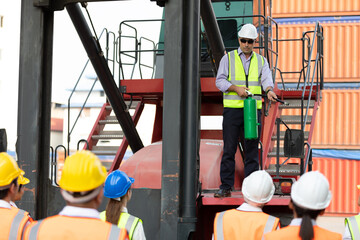 male engineer standing on crane car using fire extinguisher with factory workers in containers...