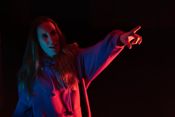 Young beautiful caucasian woman pointing on dark background with neon color lights.