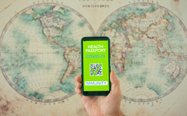 Human hand shows digital health passport app for people vaccinated against coronavirus, background with world map