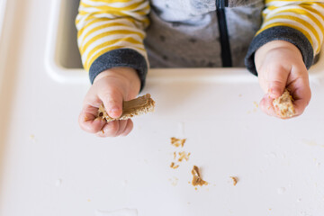 Toddler hands holding strips of bread with peanut butter on them; early exposure to allergenic...