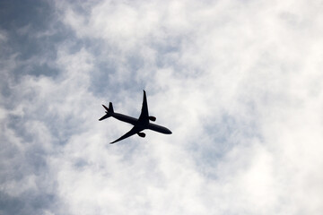 Silhouette of airplane flying in blue sky with white clouds. Passenger plane at flight, travel concept