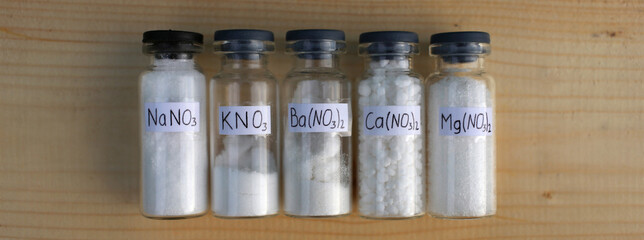 White salts, nitrates of different metals in glass jars with formulas.