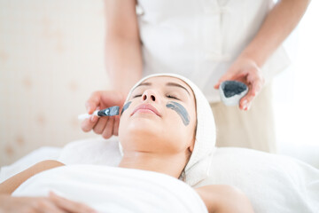The spa staff is applying the cream to the face. Young woman is masking her face in a spa salon. A young Caucasian woman spa massage at beauty spa salon.