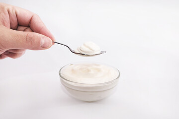  Hand holds a spoon with sour cream on white.