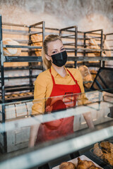 Beautiful blond female worker with protective face mask working in bakery.