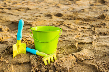 Fototapeta na wymiar Children`s beach toys on the sand playground. Green metal spade, pail and rake.
