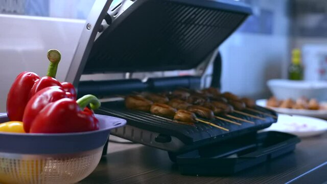 Grilling vegetables. Hot electric grill. Nice female hand  rotating mushrooms on a hot grill. Mushrooms, big peppers.Cooking, grilling, close-up.