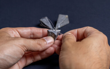 Fototapeta premium Fishing line and sinker being handled by the hand of a brown man demonstrating how to correctly thread the line on a black and dark background. Used for fishing and family leisure.