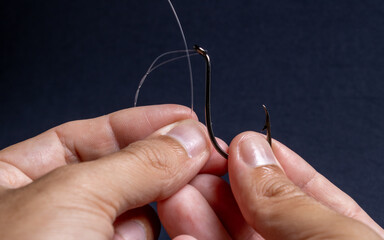 Fishing line and hook being handled by the hands of a brown man demonstrating how to thread the...