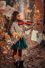 A beautiful girl plays the violin among the autumn orange foliage in the forest and with music...