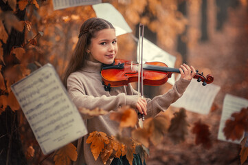 A beautiful girl plays the violin among the autumn orange foliage in the forest and with music...