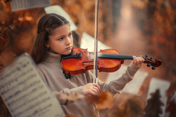 A beautiful girl plays the violin among the autumn orange foliage in the forest and with music...
