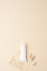 White tube of cosmetic cream with flowers on pastle beige background. Flat lay, copy space