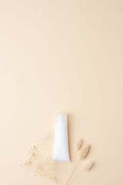 White tube of cosmetic cream with flowers on pastle beige background. Flat lay, copy space