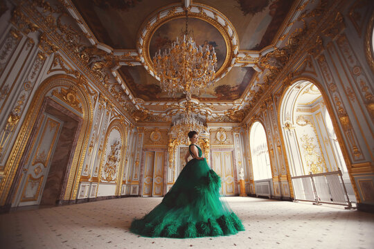 Portrait of a beautiful young girl in a haute couture green dress standing in a luxurious gold interior.