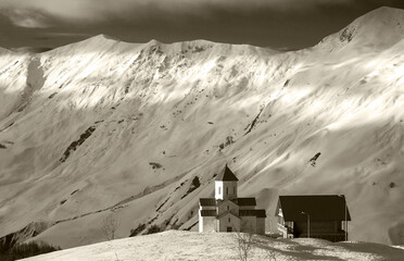 mountain hut and small church in the snowy mountains under high ridge in black and white 