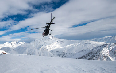 helicopter flying away towards snowy mountain peaks 