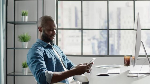 Thoughtful black man in denim chats on smartphone in office