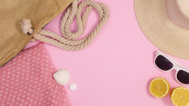 Summer beach bag, hat and accessories move on pastel pink background with copy space. Stop motion flat lay