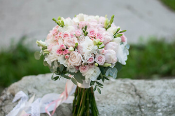 Obraz na płótnie Canvas Beautiful bridal bouquet of white and pink flowers and greenery, decorated with long silk ribbon lies on a gray textural background.