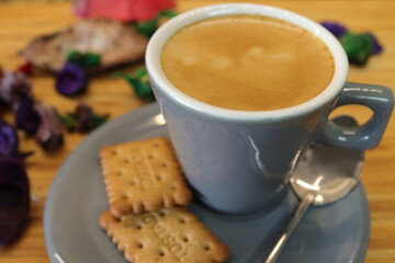 Café expreso en taza gris con galletas y fondo con flores.