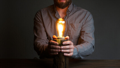 A man holds a light bulb in his hands. Concept Idea. Table lamp. Wooden decorative lamp. Night light in the dark.