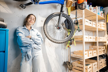 Portrait of a young handywoman standing relaxed in the workshop or garage with bicycle and wooden...