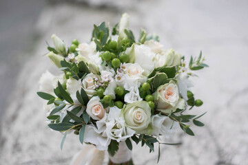 Beautiful bridal bouquet of white flowers and greenery, decorated with long silk ribbon lies on a gray textural background.