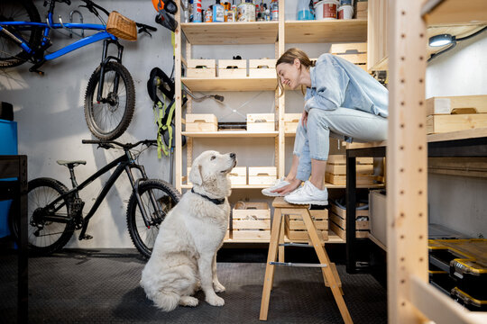 Woman playing with her huge white dog in the workshop or garage at home