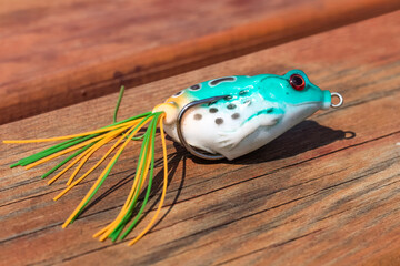 Fishing hook with a bayman in the shape of a frog. Fishing bait on wooden background. Male Hobbies...