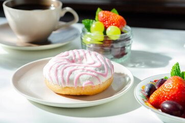 Delicious doughnut topped with white and pink icing served with coffee and fresh fruits