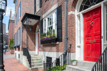 Fototapeta na wymiar Boston, MA - April 8 2021: Front of brownstone apartment brick building with windows, shutters, stoops and planters in Boston