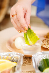 A woman's hand dips a leaf of lettuce in salt water during the Pesach Seder.