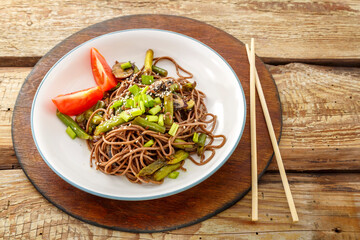 Soba with mushrooms and sesame seeds in a plate on a wooden stand on the table next to chopsticks.