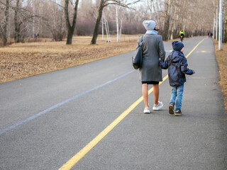 Fototapeta premium Mom and son are walking in the spring city park. Cloudy day. Back view.