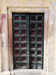 A decorative dark color door gate with square pattern design of local residence in narrow alley between colourful houses in Varanasi, India.