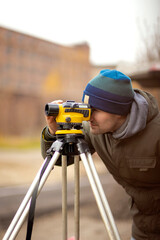 Design engineer surveyor with equipment for determining the ground level with a level on a construction site in the open air during geodetic work, selective focus