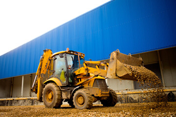 Obraz premium a powerful yellow wheeled excavator against the background of rubble hills and a blue building, unloads rubble. Heavy equipment, construction site. selective focus