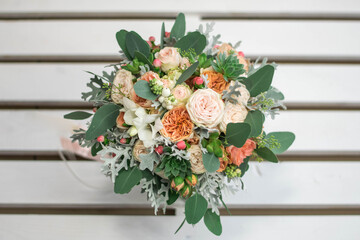 White and orange bridal bouquet of roses, freesia and eucalyphus on a gray textural background.