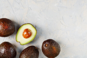 Avocado halves with whole Hass fruits on a background of gray concrete, stone or slate.