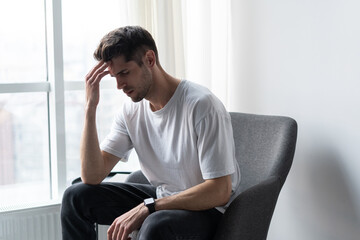 Depressed lonely man having a headache siting in an empty room