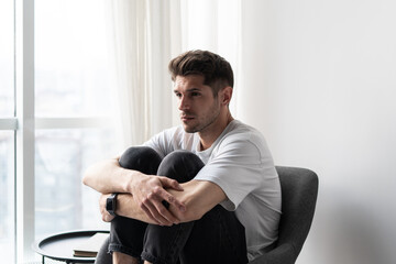 Lonely depressed man thinking about his problems siting dramatically on the chair holding his knees 
