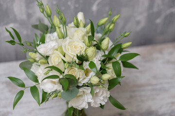 Obraz na płótnie Canvas Beautiful bridal bouquet of white flowers and greenery, decorated with long silk ribbon lies on a gray textural background. Copy space