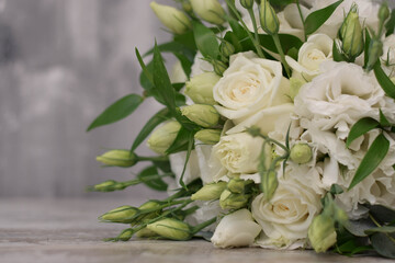 Beautiful bridal bouquet of white flowers and greenery, decorated with long silk ribbon lies on a gray textural background. Copy space