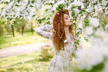 Curly woman with the hat posing in blooming spring park. The concept of relax, travel, paradise, romance and spring vacation. Fashion style.