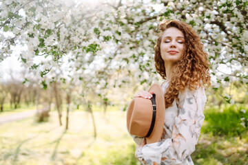 Curly woman with the hat posing in blooming spring park. The concept of relax, travel, paradise, romance and spring vacation. Fashion style.