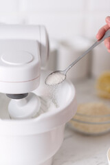Add sugar with a spoon to a working mixer.Sugar being pouring into bowl.Close-up