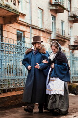A man and a woman, elegantly dressed, in 19th-century clothes, walk and talk