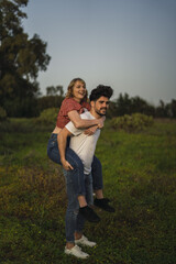 Vertical shot of a Spanish Caucasian couple in the park, him giving her a piggyback ride